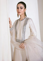 Woman wearing a traditional outfit with intricate designs in a neutral setting
