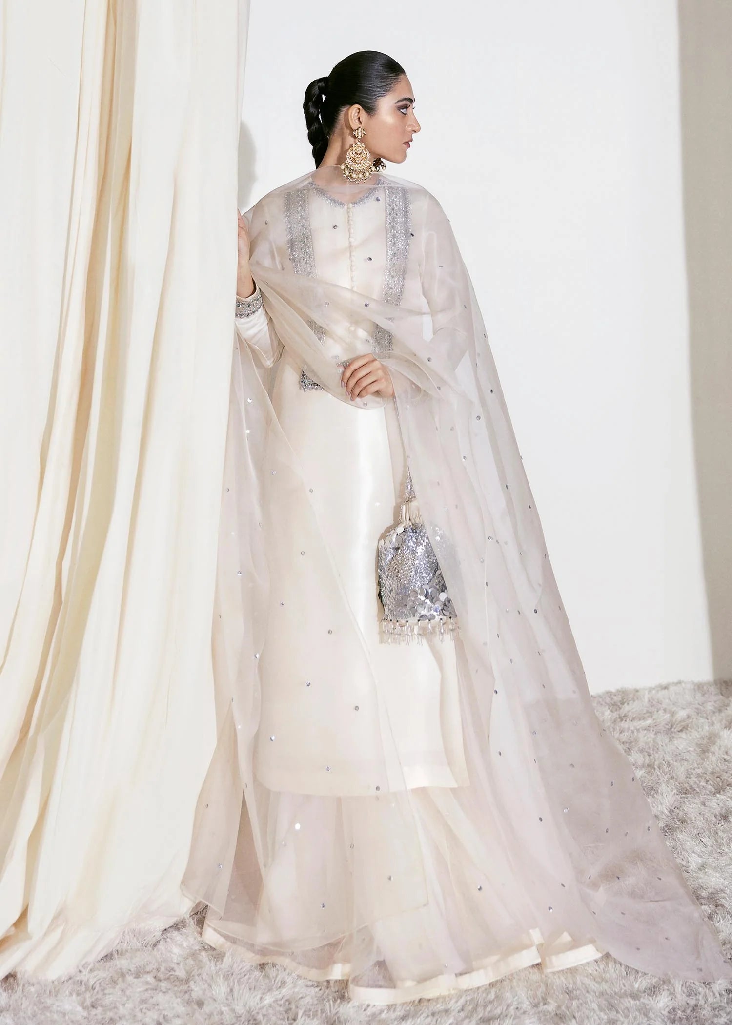Woman in a white traditional outfit with a sheer dupatta, standing against a neutral background.