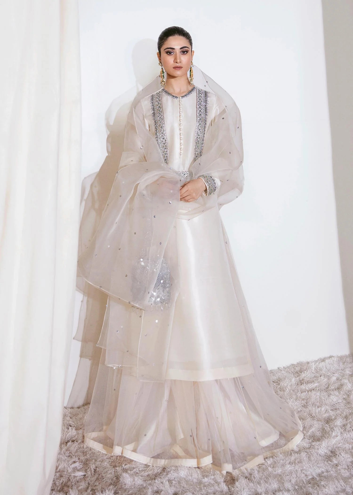 Woman wearing a white traditional outfit with a sheer dupatta on a white background