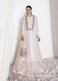 Woman in a white traditional outfit with intricate detailing, holding a decorative bag against a white curtain background.